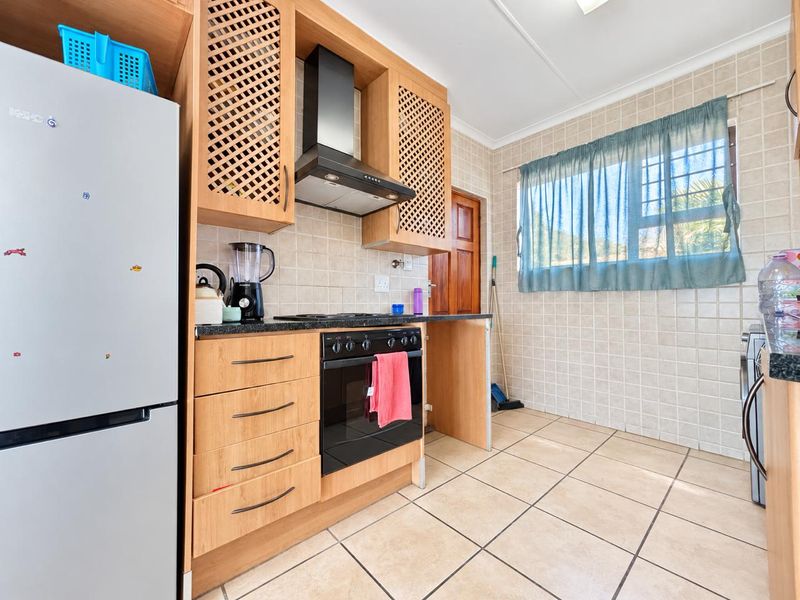 A functional kitchen featuring light wood cabinetry, tiled walls and flooring, a built-in oven, and an extractor fan.