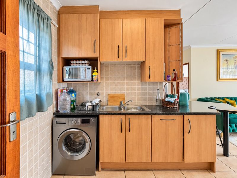 Compact kitchen featuring light wood-finish cabinetry, granite countertops, a tiled backsplash, and a dedicated space for a washing machine.