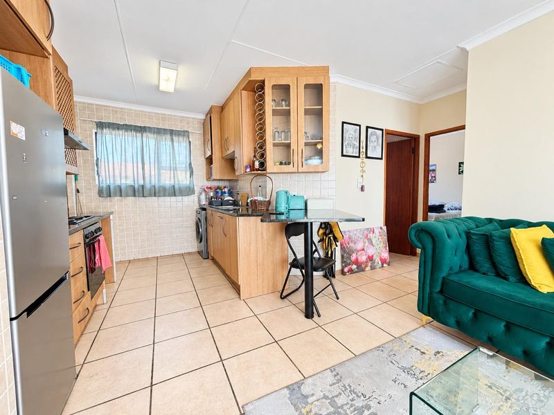 Open-plan kitchen and living area featuring tiled flooring, wooden cabinetry, and a breakfast bar, providing a functional and connected living space.