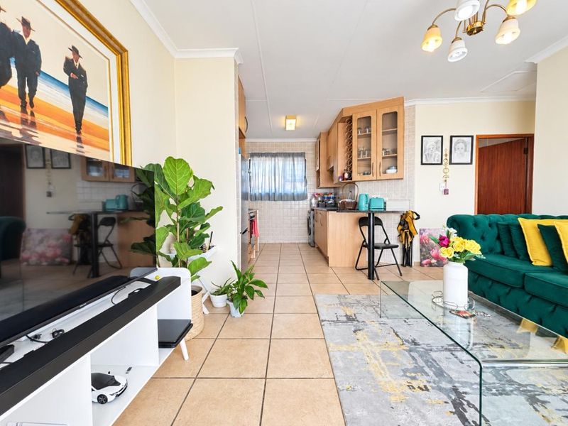 An open-plan living and kitchen area featuring tiled flooring, neutral walls, and functional built-in cabinetry, creating a cohesive and practical living space.