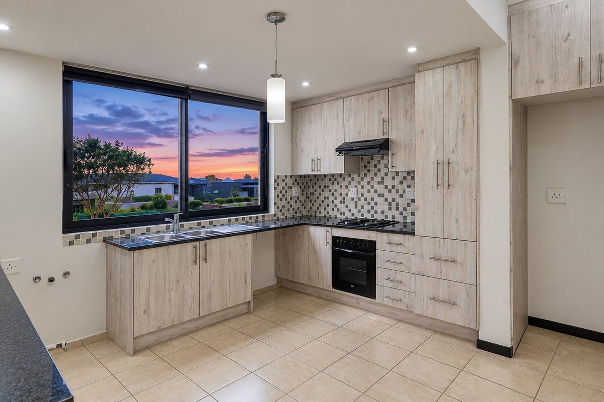 Modern kitchen featuring light wood-grain cabinetry, dark laminate countertops, built-in oven with gas hob, and a mosaic tile backsplash with large window views.