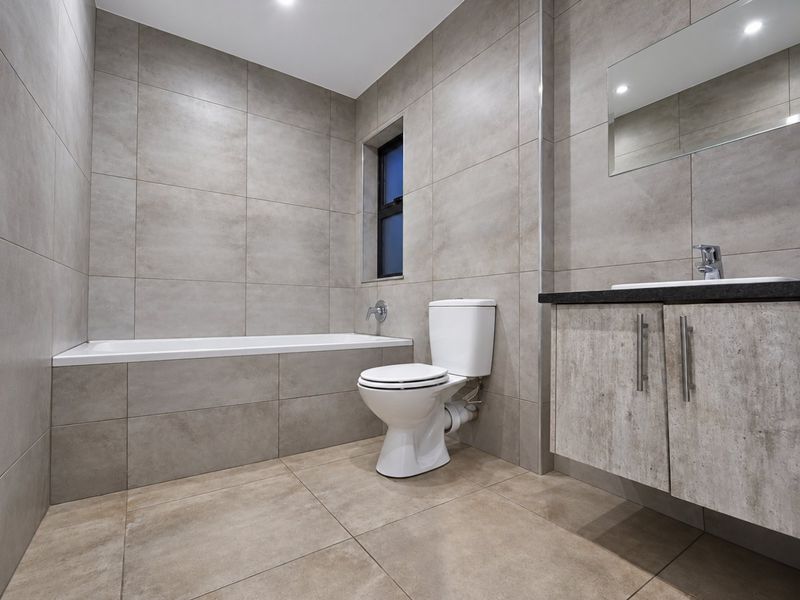 A modern, well-maintained bathroom featuring floor-to-ceiling neutral tiling, a built-in bathtub, a contemporary vanity with basin, and a wall-mounted mirror.