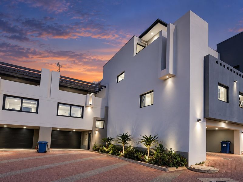 Modern multi-level residential facade featuring a paved driveway, integrated double garages, and contemporary architectural lighting at dusk.