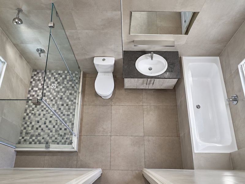Modern bathroom featuring a glass-enclosed shower, separate bathtub, vanity with stone countertop, and neutral large-format floor tiles.