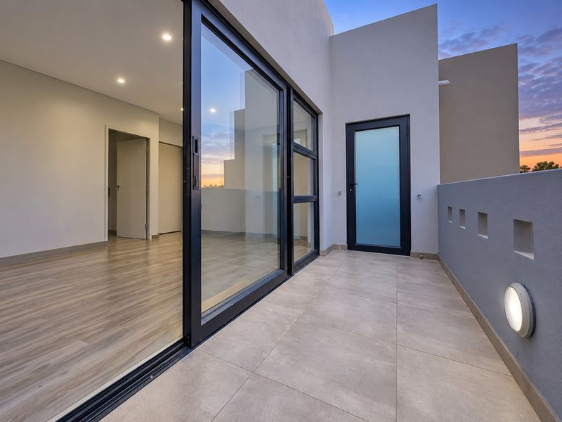 A modern, clean balcony featuring large sliding glass doors, tiled flooring, and contemporary lighting, providing a seamless transition to the interior living space.