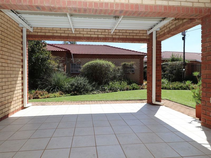 A covered outdoor patio area featuring brick pillars and tiled flooring, overlooking a well-maintained garden space.