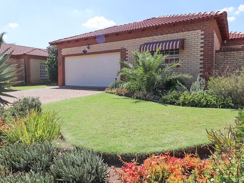 Front view of a well-maintained townhouse featuring a brick facade, tiled roof, paved driveway, and a double garage with an established garden.