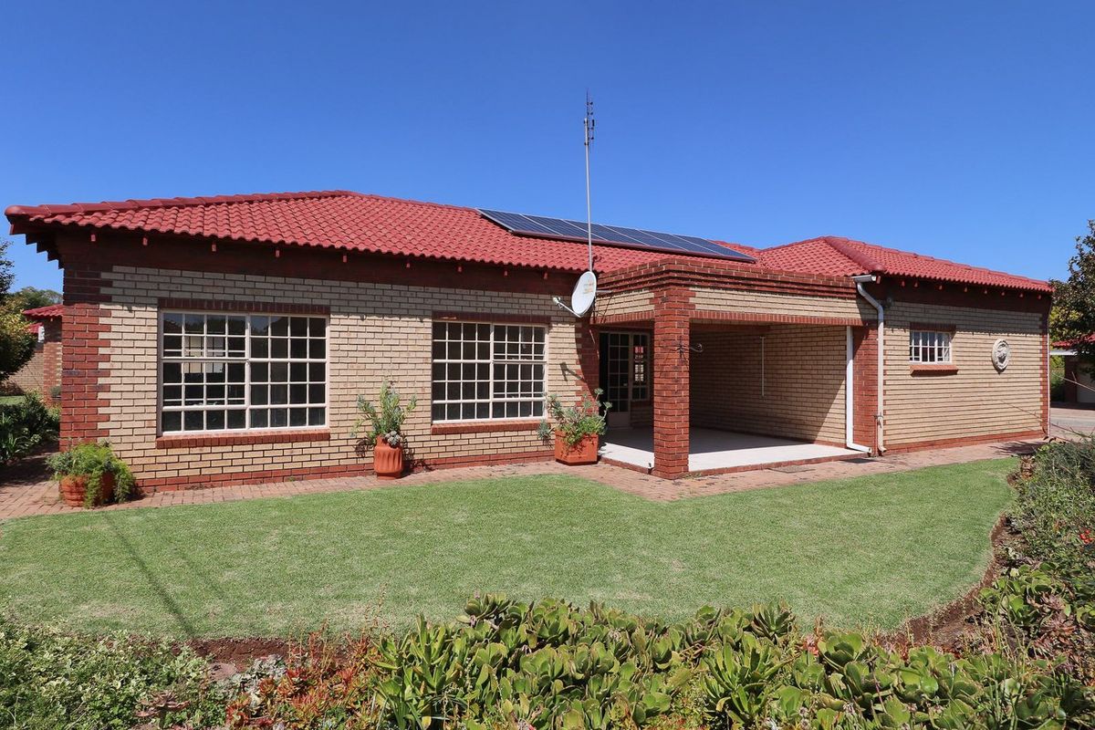 Rear view of a brick townhouse featuring a red tiled roof, solar panels, and a covered patio area overlooking a landscaped garden.