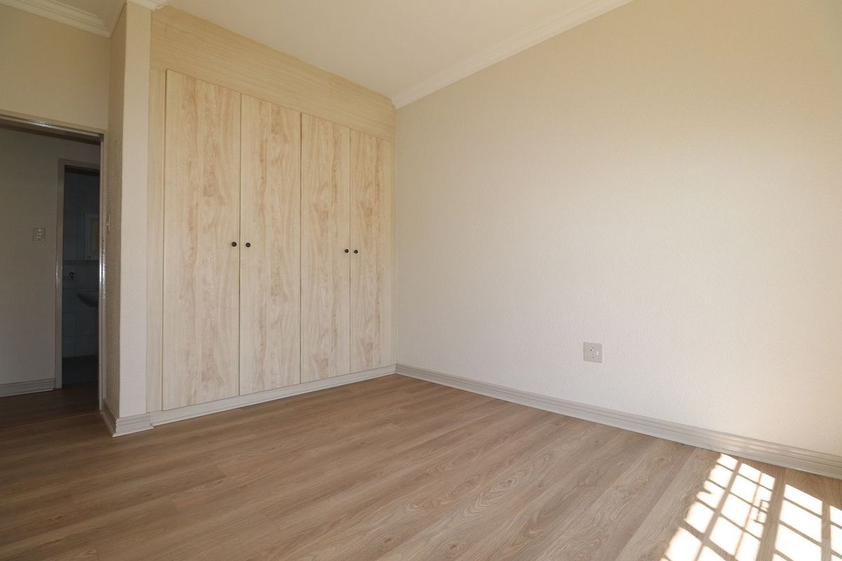 A bright, empty bedroom featuring light wood-look laminate flooring and built-in cupboards, with a doorway leading to an adjacent bathroom.