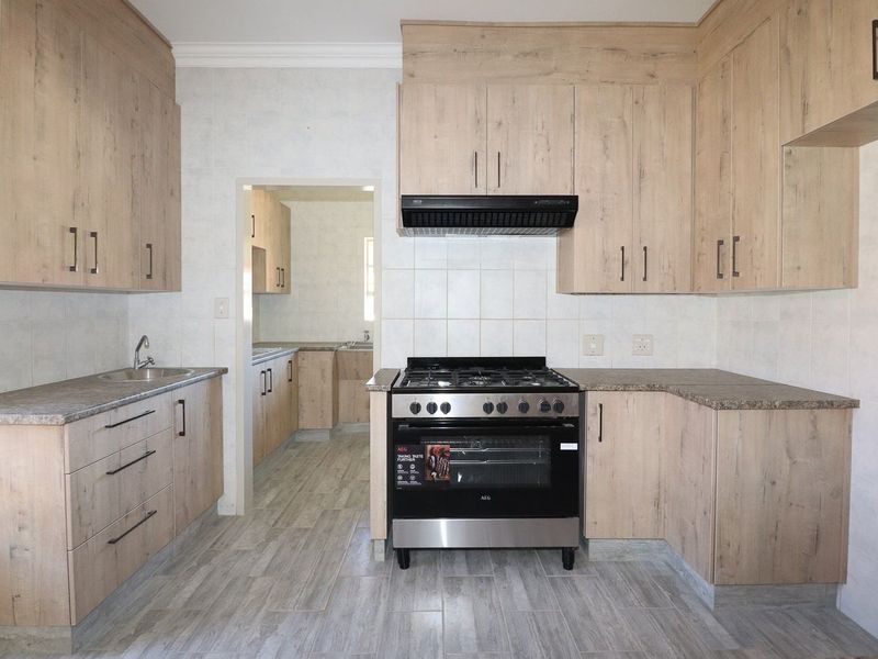 A clean, modern kitchen featuring light wood-finish cabinetry, granite-look countertops, a gas stove with extractor fan, and neutral tiled flooring throughout.