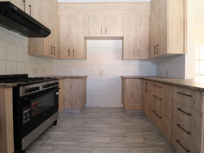 A modern kitchen featuring light wood-finish cabinetry, granite-look laminate countertops, a gas stove with extractor fan, and neutral tiled flooring.