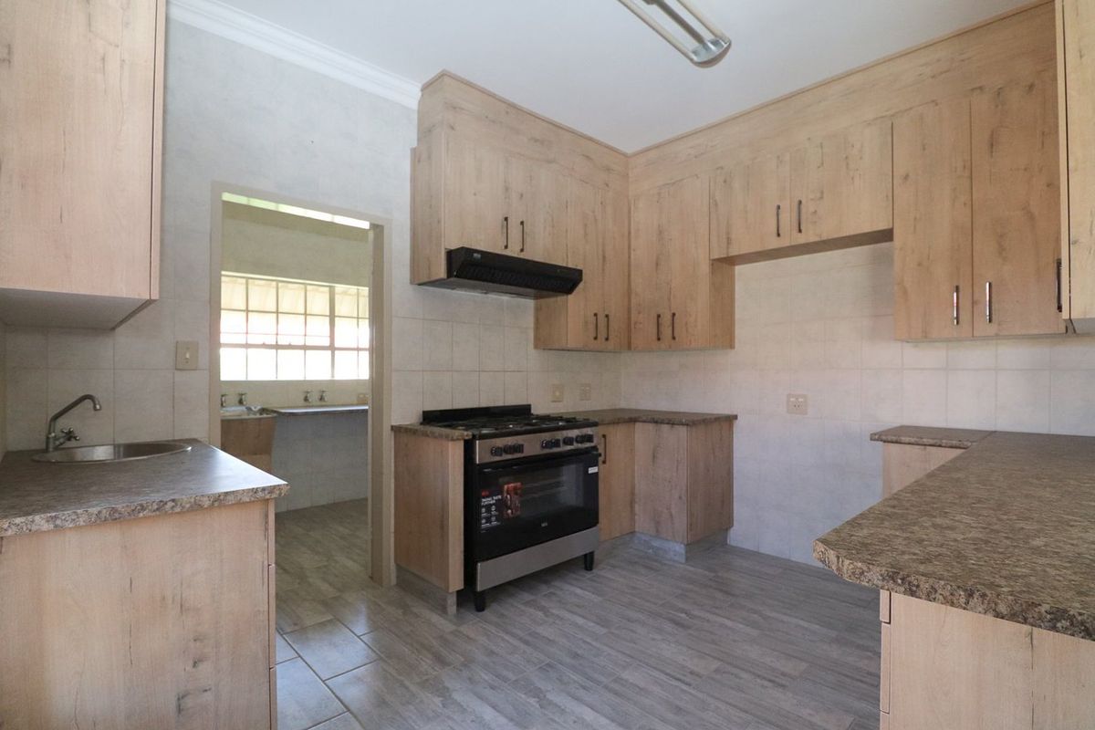 A functional kitchen featuring light wood-look cabinetry, laminate countertops, a gas stove with extractor fan, and tiled flooring, with an adjacent scullery area.