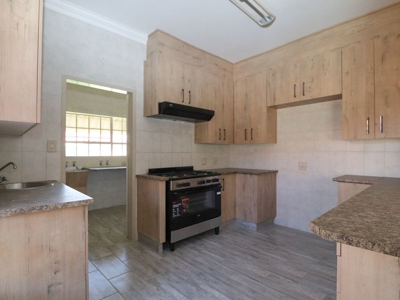 A functional kitchen featuring light wood-look cabinetry, laminate countertops, a gas stove with extractor fan, and tiled flooring, with an adjacent scullery area.