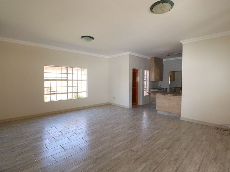 Spacious open-plan living area featuring tiled flooring, neutral walls, and an integrated kitchen with breakfast bar, offering a versatile layout for modern living.
