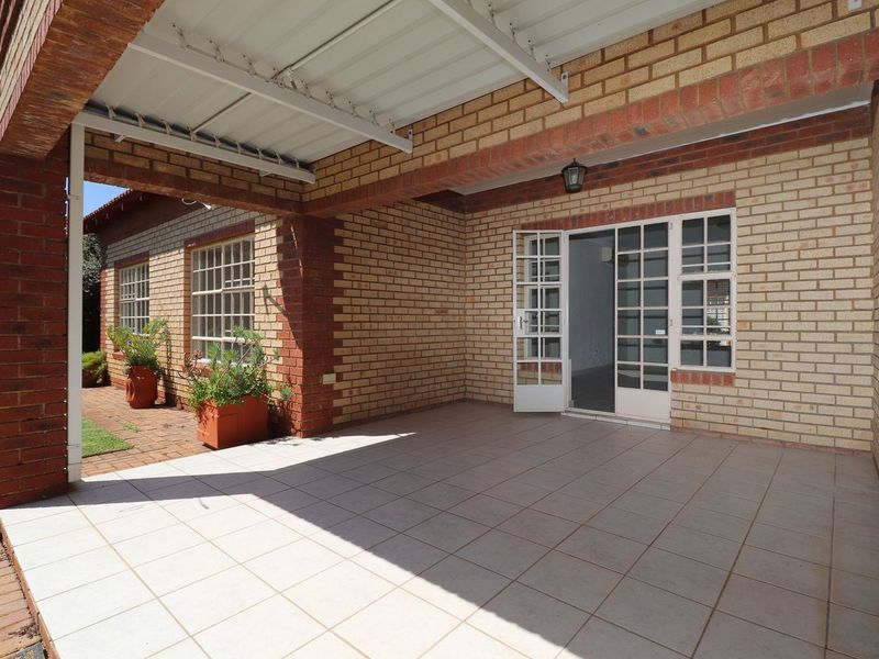 A spacious covered patio featuring tiled flooring, brick construction, and direct access to the interior through classic french doors.