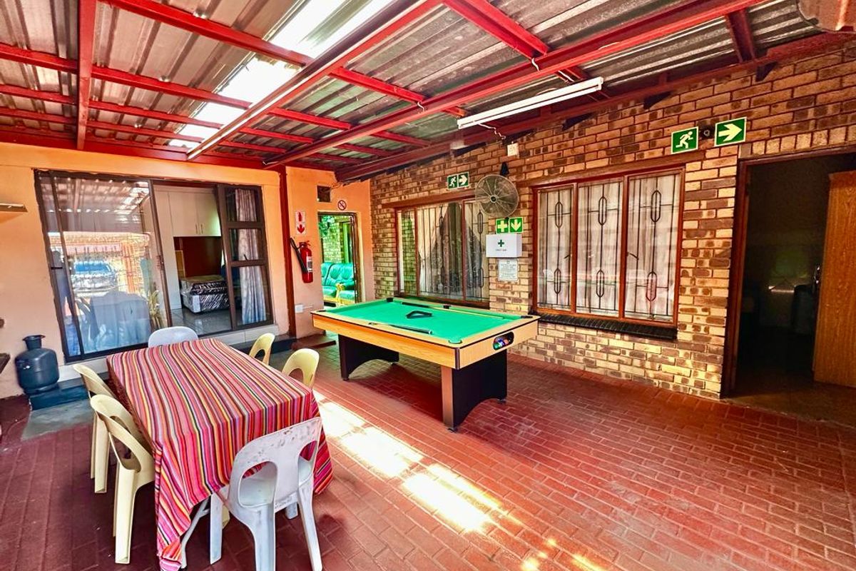 Covered outdoor patio area featuring exposed brick walls, brick paving, and a corrugated metal roof, suitable for entertainment and leisure.
