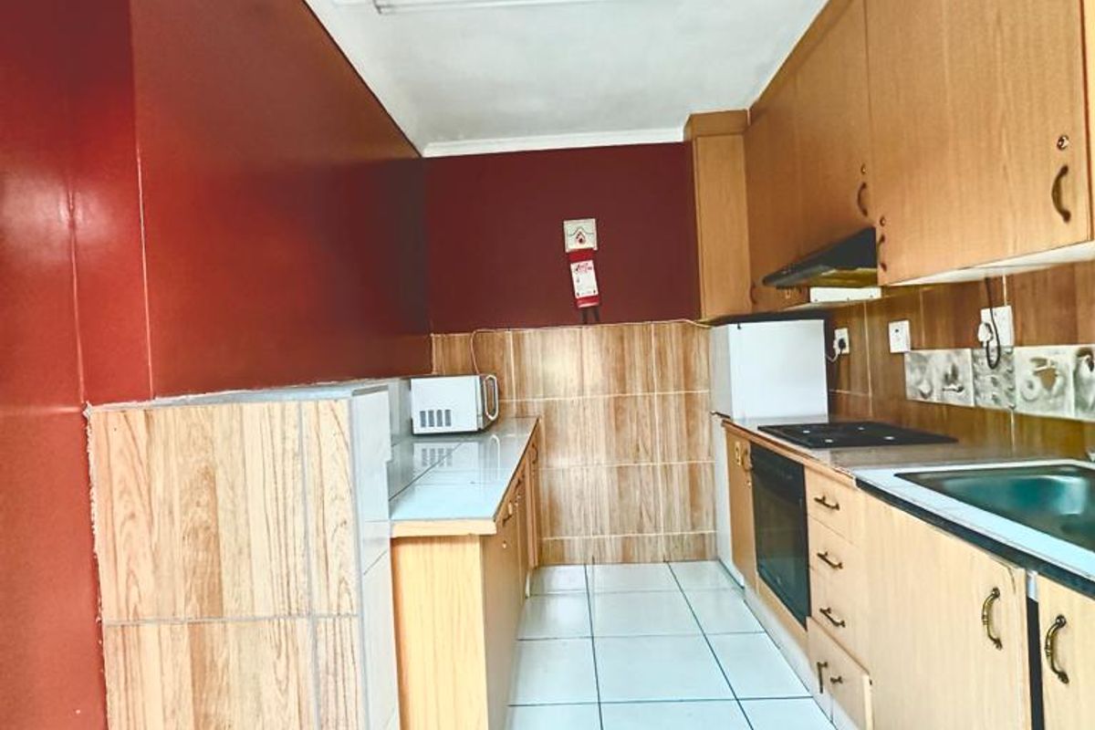 A functional galley-style kitchen featuring wood-look cabinetry, tiled backsplash, and ceramic flooring, offering a practical layout with integrated oven and hob.
