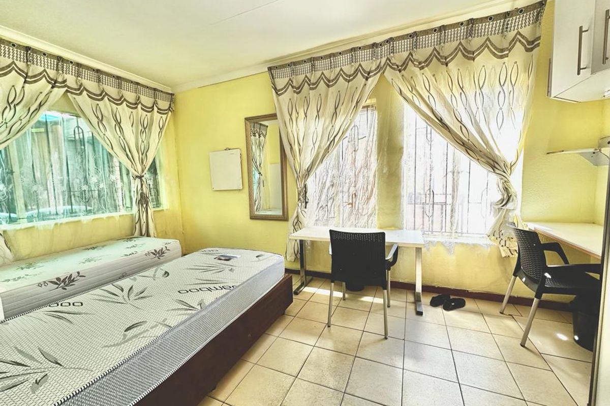 A bedroom featuring tiled flooring, built-in desk space, and security bars on the windows. The room requires cosmetic updates to improve its overall appeal.
