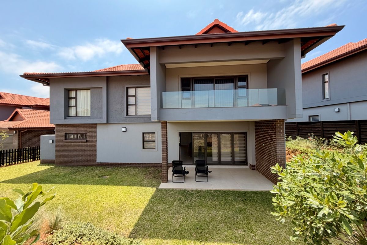 Rear view of a modern two-story house featuring a covered patio, a glass-balustrade balcony, and a well-maintained garden area.