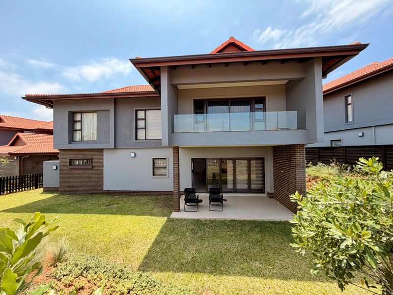 Rear view of a modern two-story house featuring a covered patio, a glass-balustrade balcony, and a well-maintained garden area.