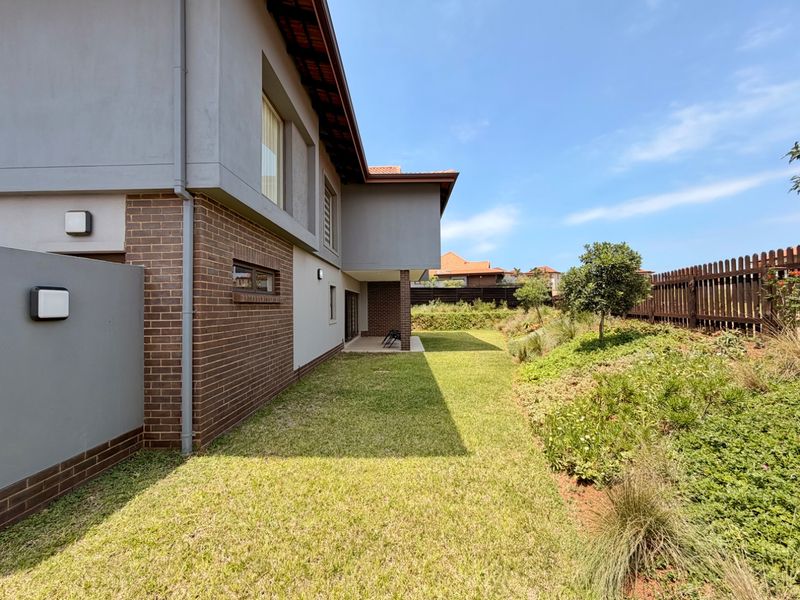 A well-maintained rear exterior view of the house featuring a brick and plaster facade, a neat lawn, and a landscaped garden with timber fencing.