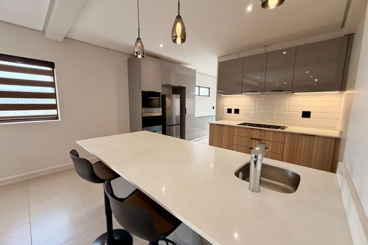 Modern kitchen featuring a large island with quartz countertops, high-gloss cabinetry, built-in appliances, and stylish pendant lighting.