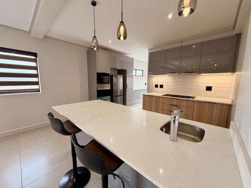 Modern kitchen featuring a large island with quartz countertops, high-gloss cabinetry, built-in appliances, and stylish pendant lighting.