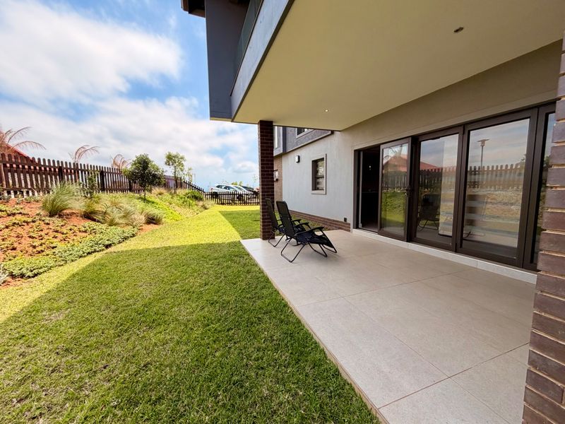A covered patio area featuring large format floor tiles, recessed lighting, and sliding glass doors that provide seamless access to the landscaped garden.