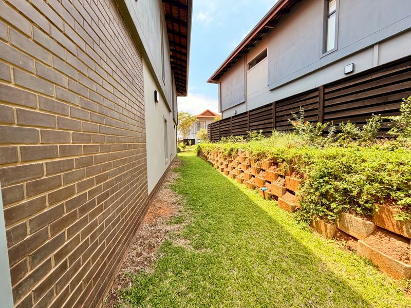 A side garden pathway featuring a manicured lawn, a tiered brick retaining wall with integrated landscaping, and a timber privacy fence between two properties.