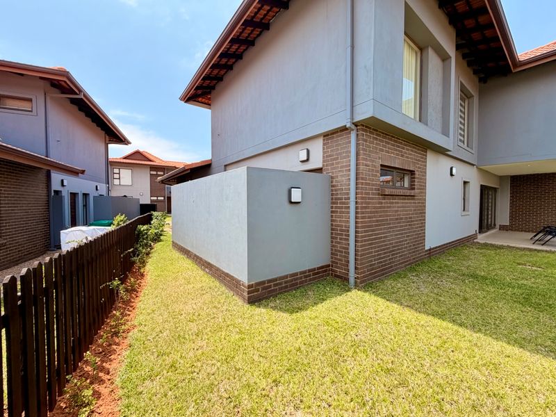 A view of the rear exterior of the house featuring a well-maintained lawn, brick and plaster facade, and a perimeter picket fence.