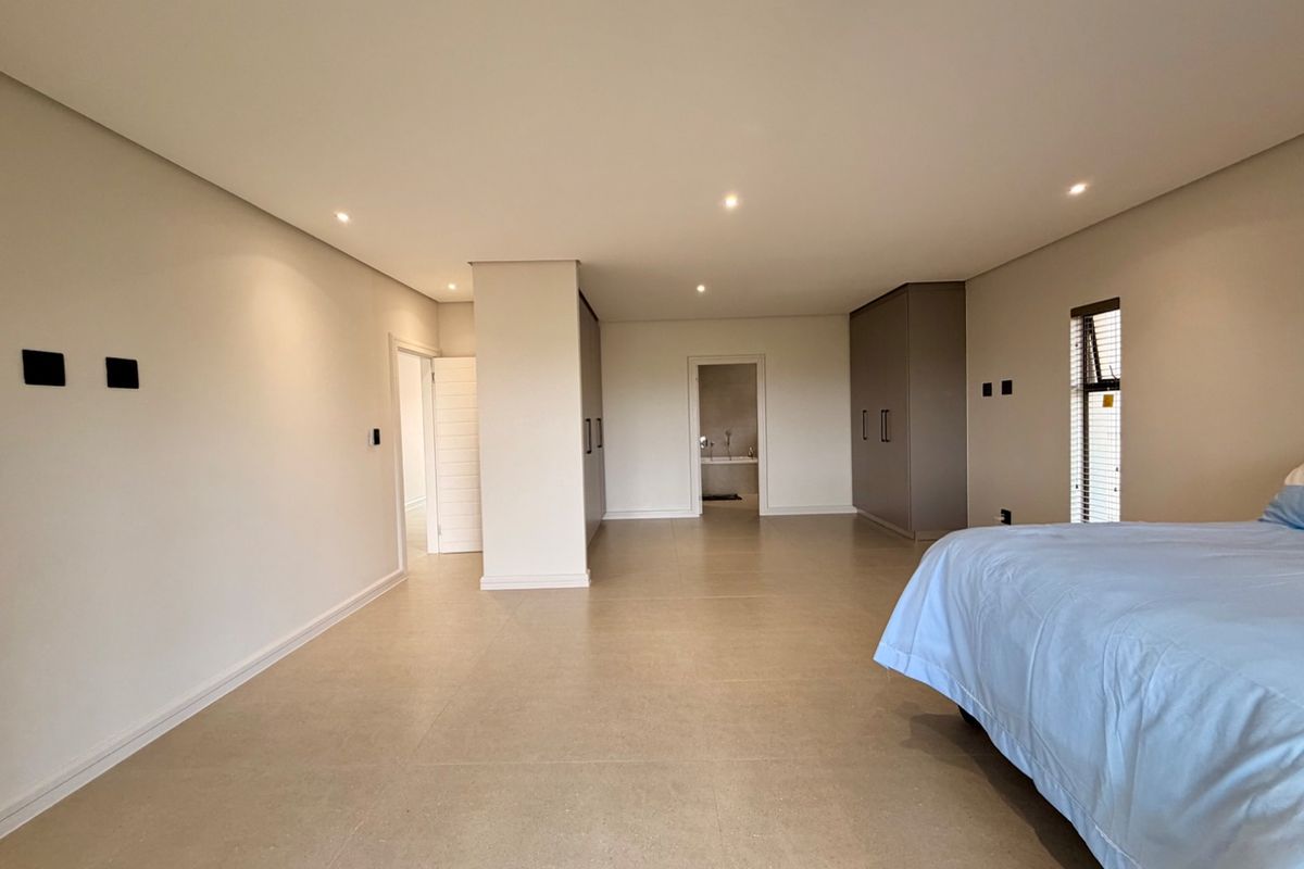 Spacious bedroom featuring neutral tiled flooring, recessed downlighting, and extensive built-in cupboard storage with an en-suite bathroom visible through the doorway.