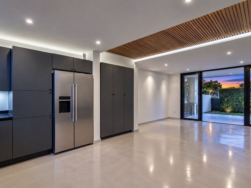 Modern open-plan living area featuring polished concrete floors, sleek dark cabinetry, integrated appliances, and a striking slatted timber ceiling with seamless indoor-outdoor flow.