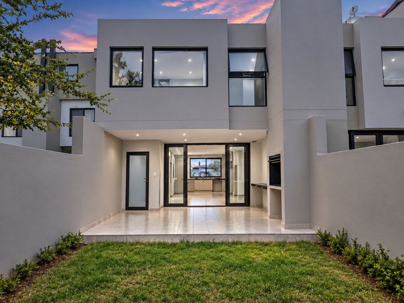 Modern rear exterior featuring a tiled patio with a built-in braai, sliding glass doors leading to the interior, and a well-maintained garden area.