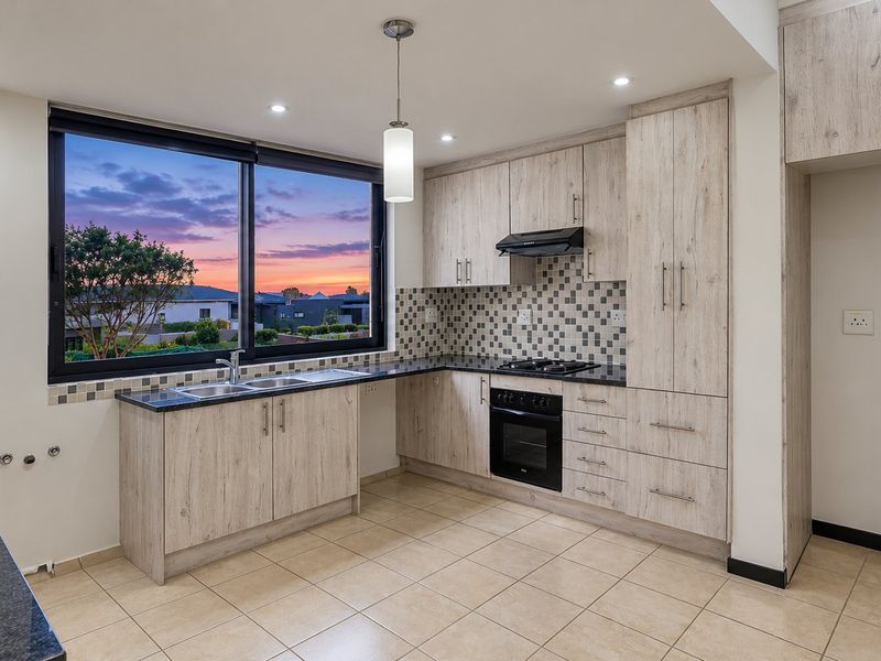 Modern kitchen featuring light wood-grain cabinetry, dark laminate countertops, built-in oven with gas hob, and a mosaic tile backsplash with large window views.