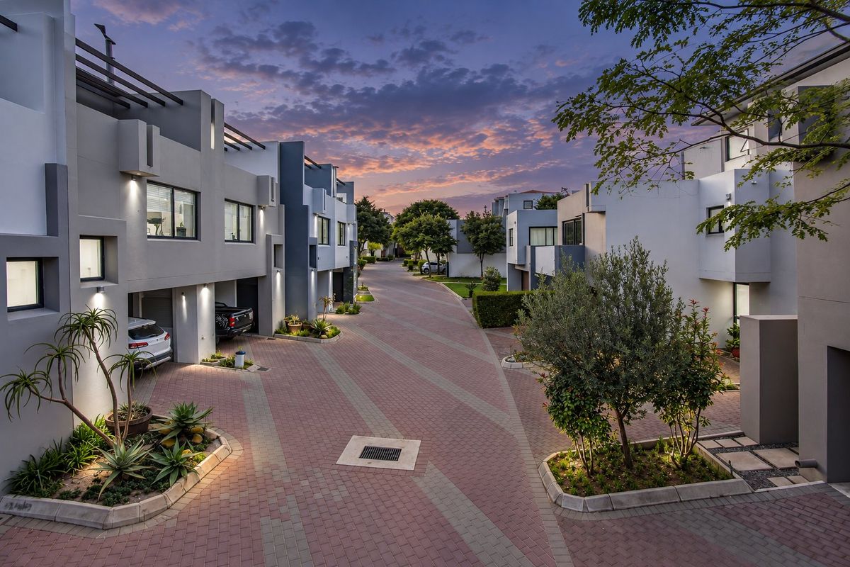 A well-maintained modern residential complex street view featuring paved driveways, integrated garages, and landscaped garden beds under a sunset sky.