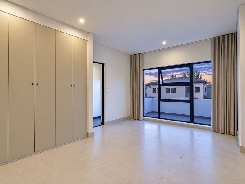 A bright, modern bedroom featuring neutral tiled flooring, ample built-in cupboard space, and large aluminium-framed windows with access to a balcony.
