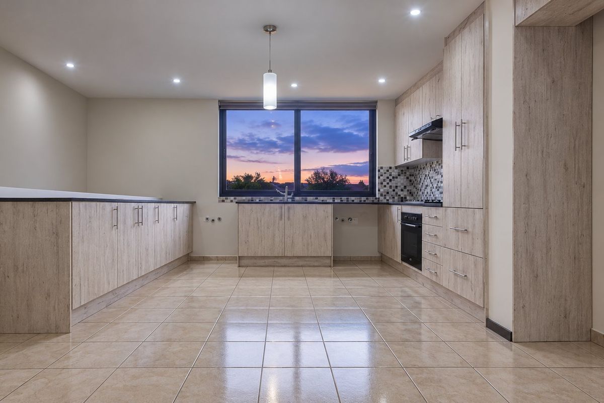 Modern, spacious kitchen featuring light wood-grain cabinetry, tiled flooring, built-in oven, extractor fan, and a mosaic backsplash with a large window.