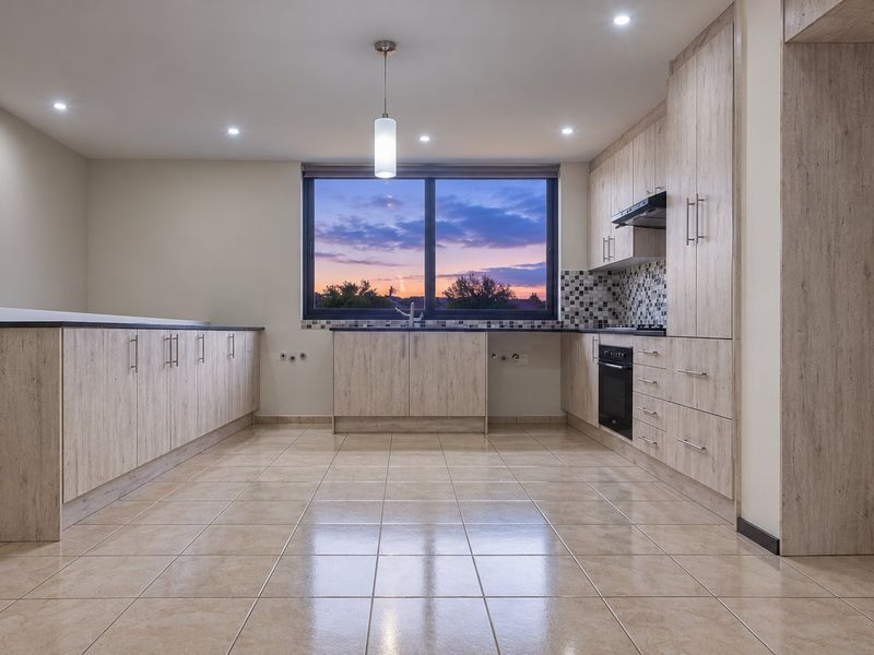 Modern, spacious kitchen featuring light wood-grain cabinetry, tiled flooring, built-in oven, extractor fan, and a mosaic backsplash with a large window.
