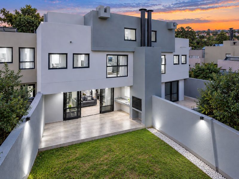 Modern rear elevation featuring a tiled patio, built-in braai, and a private garden with perimeter wall lighting.