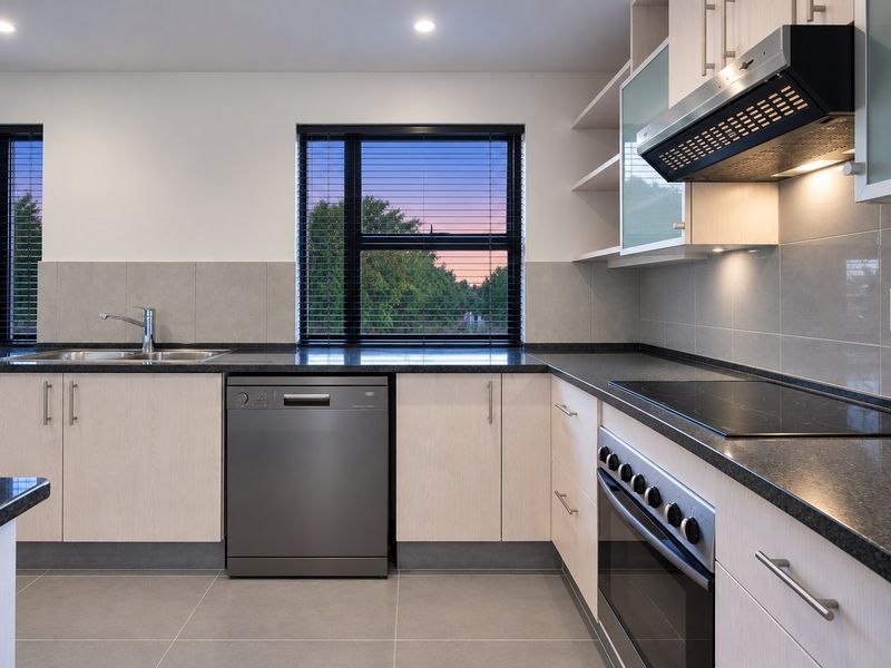 Modern kitchen featuring light wood cabinetry, dark granite countertops, integrated appliances, and a tiled backsplash with views of the outdoors.