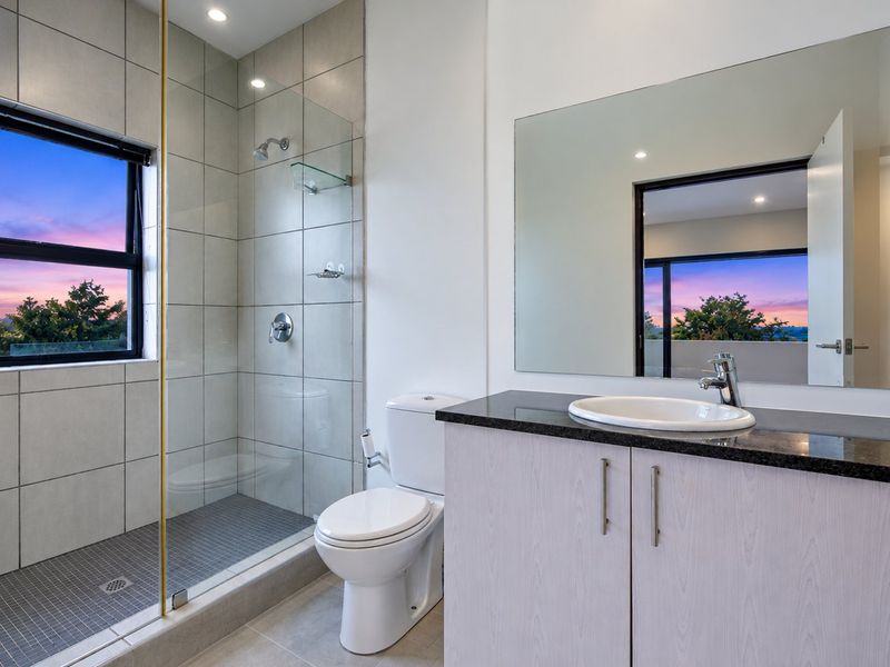 Modern bathroom featuring a walk-in shower with glass screen, vanity with granite countertop, and large wall mirror, offering a clean and contemporary aesthetic.