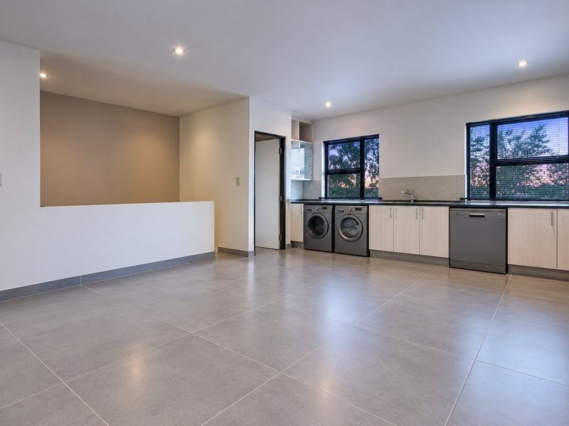Spacious open-plan kitchen and living area featuring modern tiled flooring, neutral cabinetry, and integrated laundry appliances in a clean, well-maintained setting.
