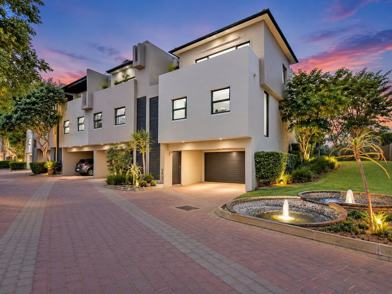 Modern multi-story townhouse exterior featuring a paved driveway, integrated double garage, and a beautifully landscaped front garden with a decorative water feature.