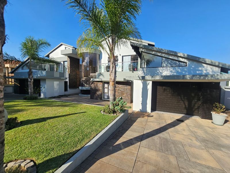 Modern architectural front elevation featuring stone cladding, expansive glass elements, a paved driveway, and a well-maintained lawn.