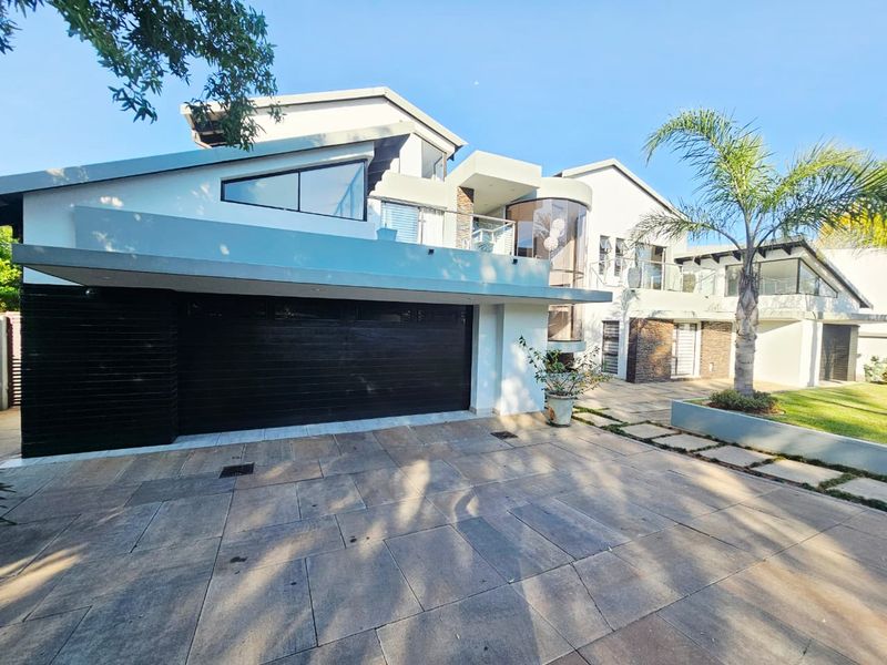 Modern multi-level residential property featuring a double garage, paved driveway, and contemporary architectural design with glass balcony balustrades.