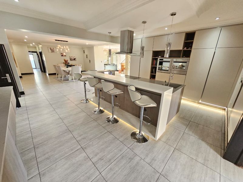 Modern open-plan kitchen and dining area featuring a large island with breakfast bar, integrated appliances, sleek cabinetry, and contemporary tiled flooring throughout.