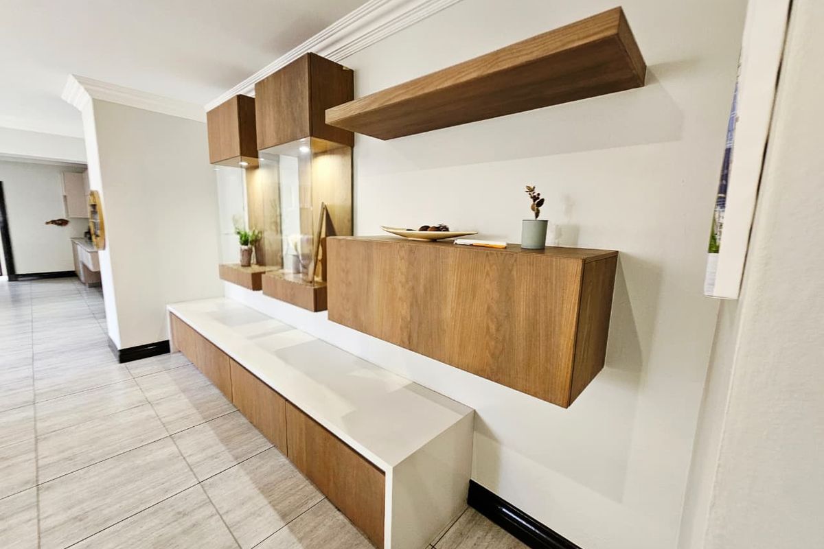 Modern living area featuring custom built-in wooden cabinetry, floating shelves, and sleek tiled flooring with elegant crown molding details.