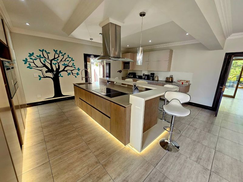 Modern kitchen featuring a large central island with integrated hob, stainless steel extractor fan, ample cabinetry, and stylish undercounter lighting.