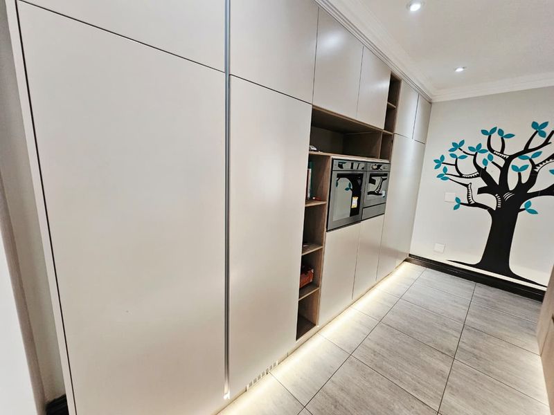 Modern kitchen featuring sleek floor-to-ceiling cabinetry, integrated oven and microwave, tiled flooring, and ambient under-cabinet lighting.
