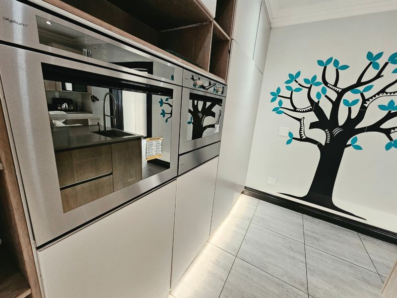 Modern kitchen featuring integrated stainless steel ovens, sleek cabinetry with under-cabinet lighting, and contemporary tiled flooring.